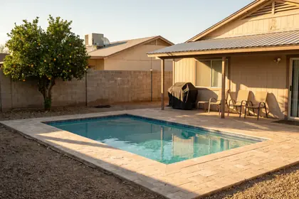 Representative stock photograph — fenced rear yard with a rectangular pool and travertine deck. Not a photograph of any asset in this panel.