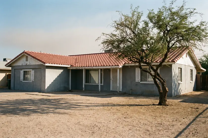 Representative stock photograph — painted stucco ranch elevation with a barrel-tile roof and mature mesquite. Not a photograph of any asset in this panel.